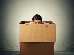 Femme qui a peur et qui se cache dans une boîte de carton.