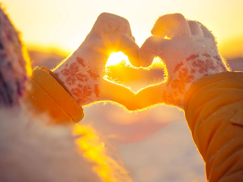 Coeur formé avec les mains, avec coucher du soleil en arrière-plan.