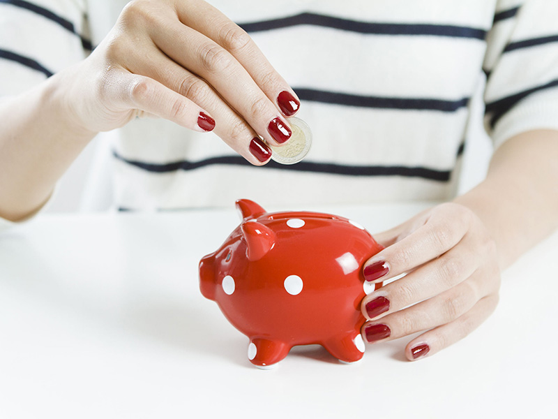 Femme déposant une pièce de monnaie dans une tirelire rouge.