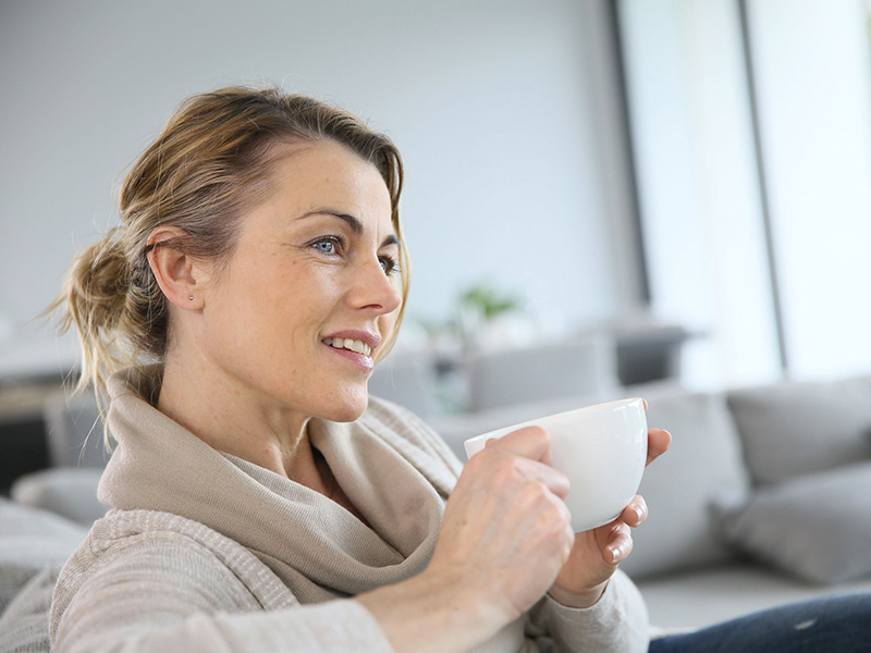 Femme pensive, tenant une tasse de café.