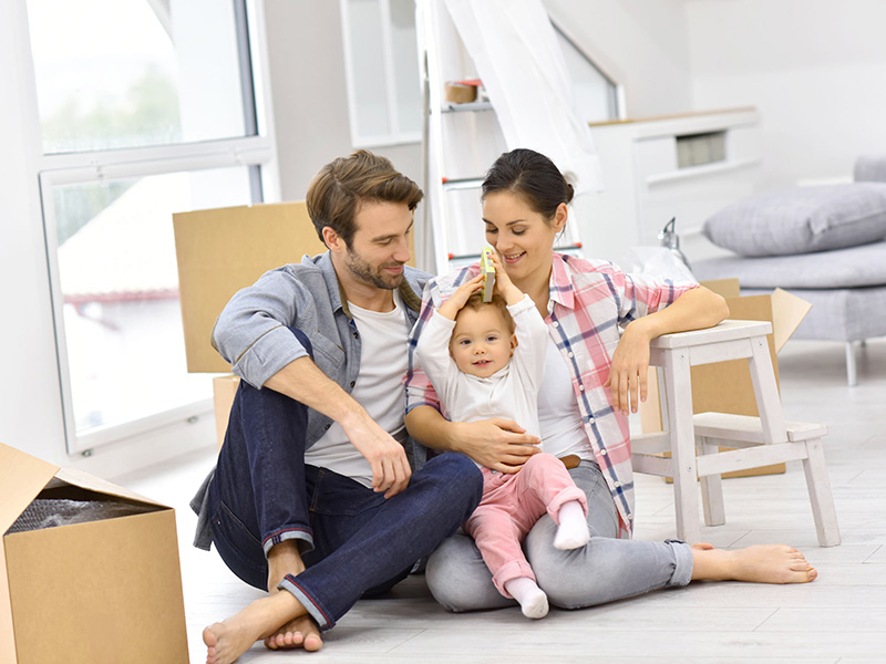 Jeune couple et leur bébé dans leur nouvelle maison, entourés de boîtes.