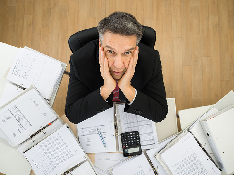 Homme inquiet devant une pile de documents.