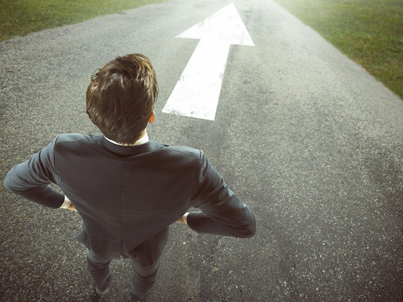 Homme d'affaires se tenant debout, face à une flèche indiquant une direction à suivre.