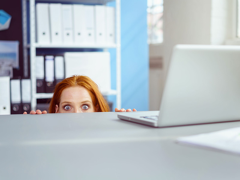 Femme se cachant derrière son bureau de travail.