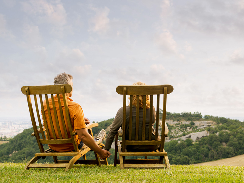 Couple de préretraités assis sur des chaises de bois dans la nature.