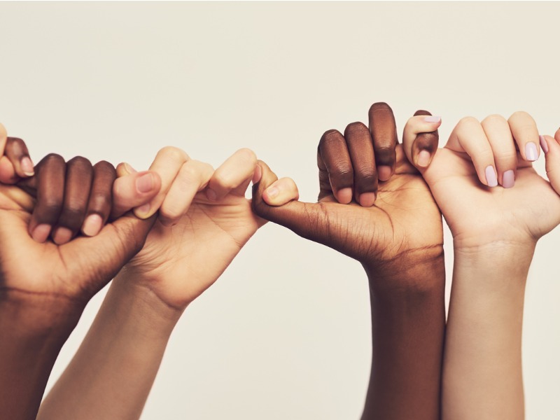 Mains de personnes de différentes origines qui se tiennent toutes par le petit doigt.