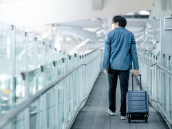 Voyageur portant un masque et tirant sa valise dans un aéroport désert.