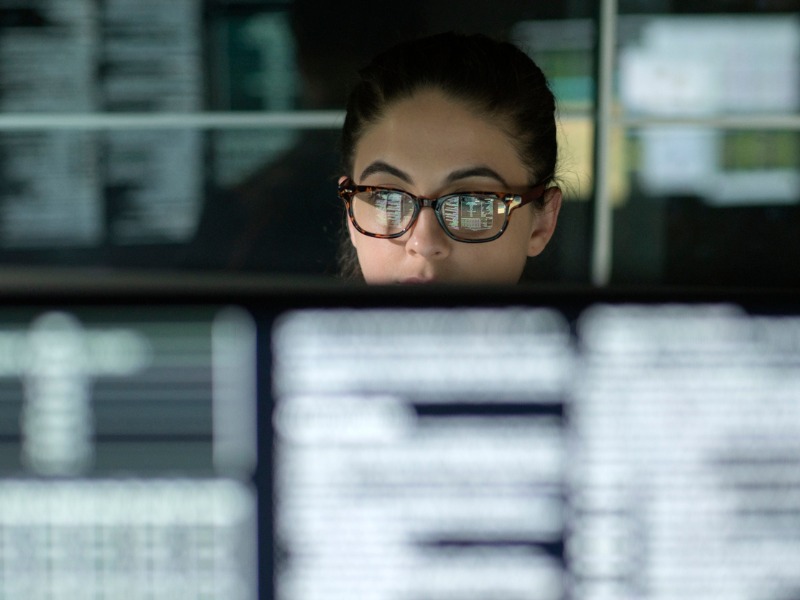 Une femme analysant des données sur plusieurs écrans d'ordinateurs.