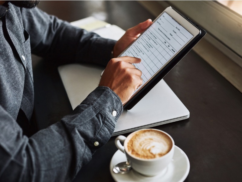 Un homme assis à une table avec un café à côté de lui. Il tient une tablette sur laquelle on voit un questionnaire.