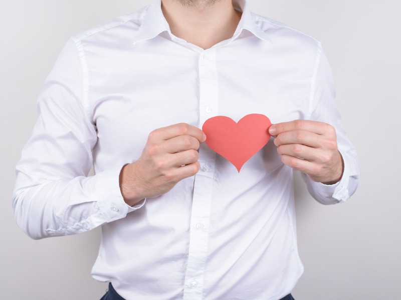 Un homme en chemise qui tient un coeur rouge en carton devant lui.